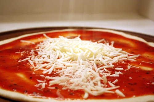adding tomato sauce and cheese to white wine honey pizza dough