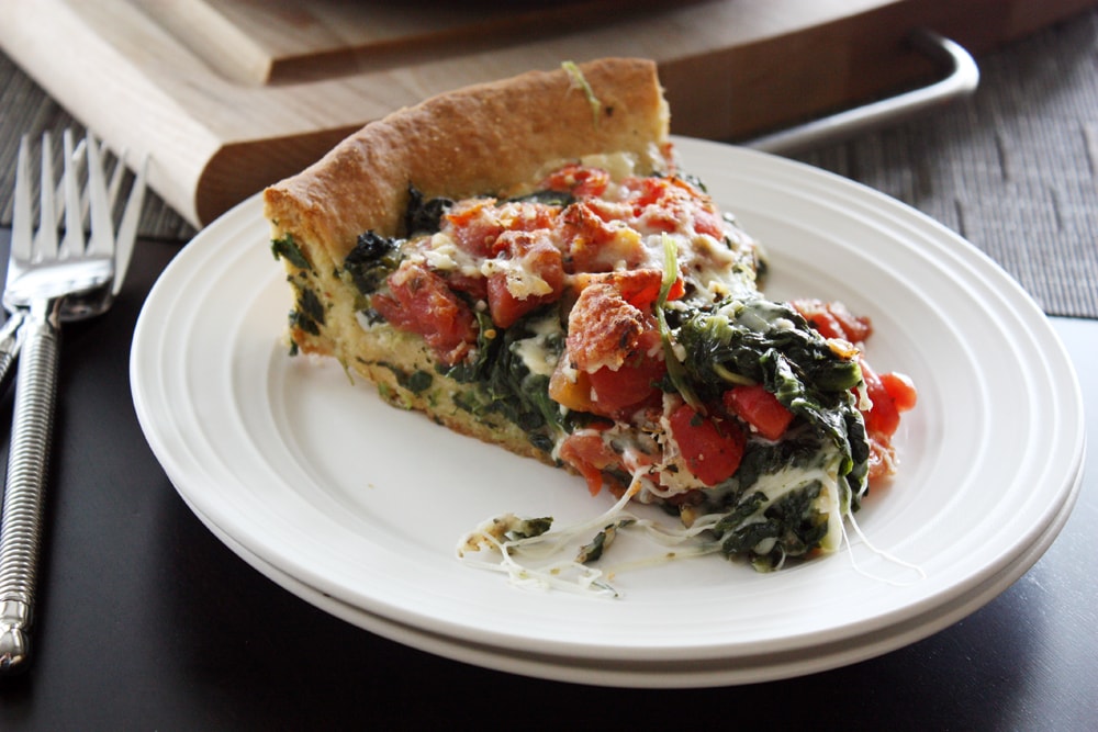 slice of deep dish spinach tomato pizza on a plate