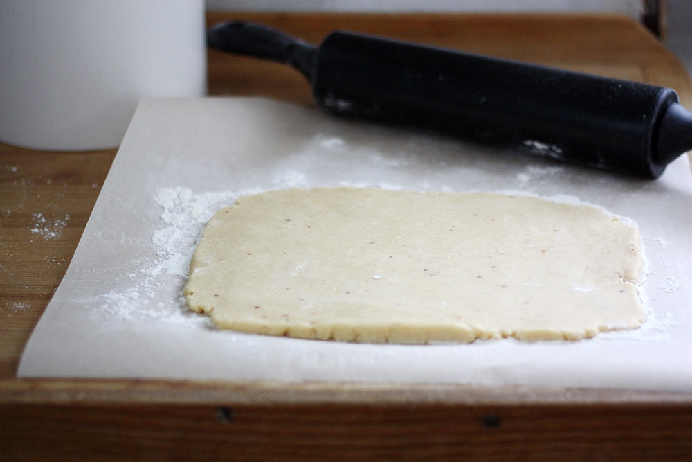 rolling out smoked gouda cheese straw dough on parchment paper