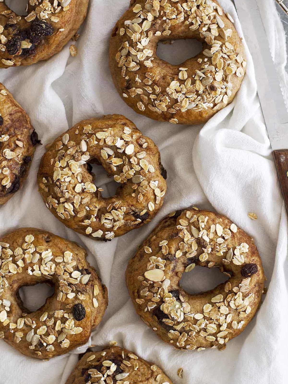 chocolate chip bagels arranged on white muslin cloth with bread knife.