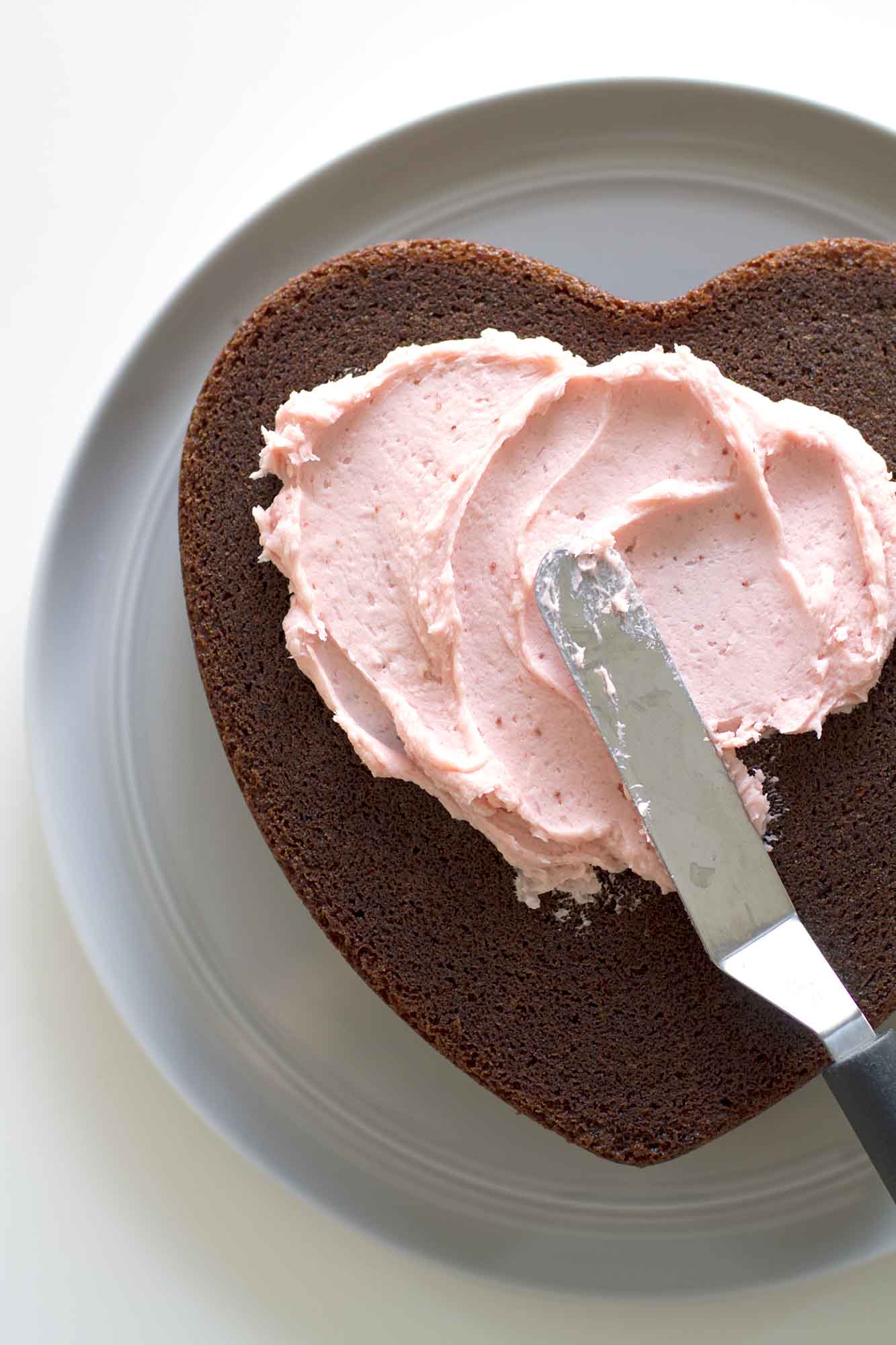 spreading pink frosting on chocolate cake