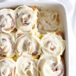 baked cinnamon rolls in white dish with cream cheese frosting.