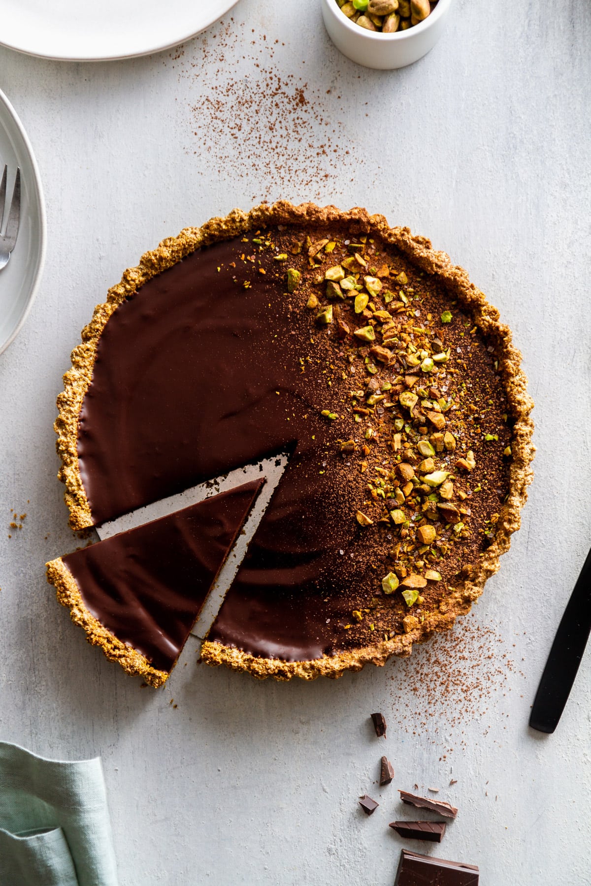 a dark chocolate pistachio tart with a slice out of it on a surface