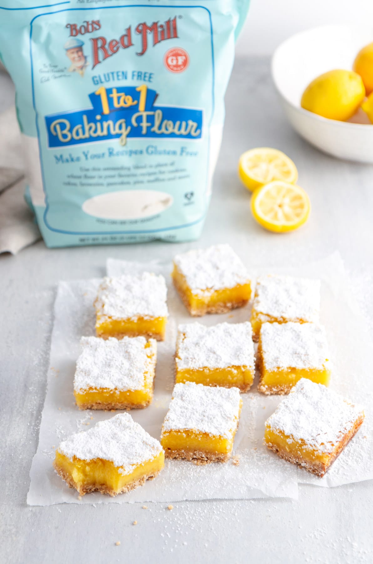 lemon bars on parchment paper with gluten free flour in the background