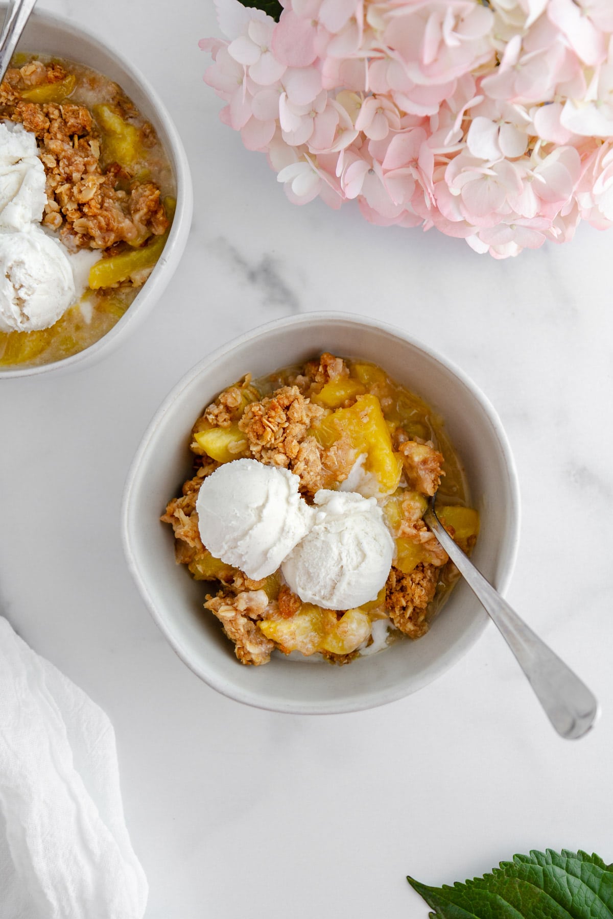 bowls of peach crisp with vanilla ice cream on a surface