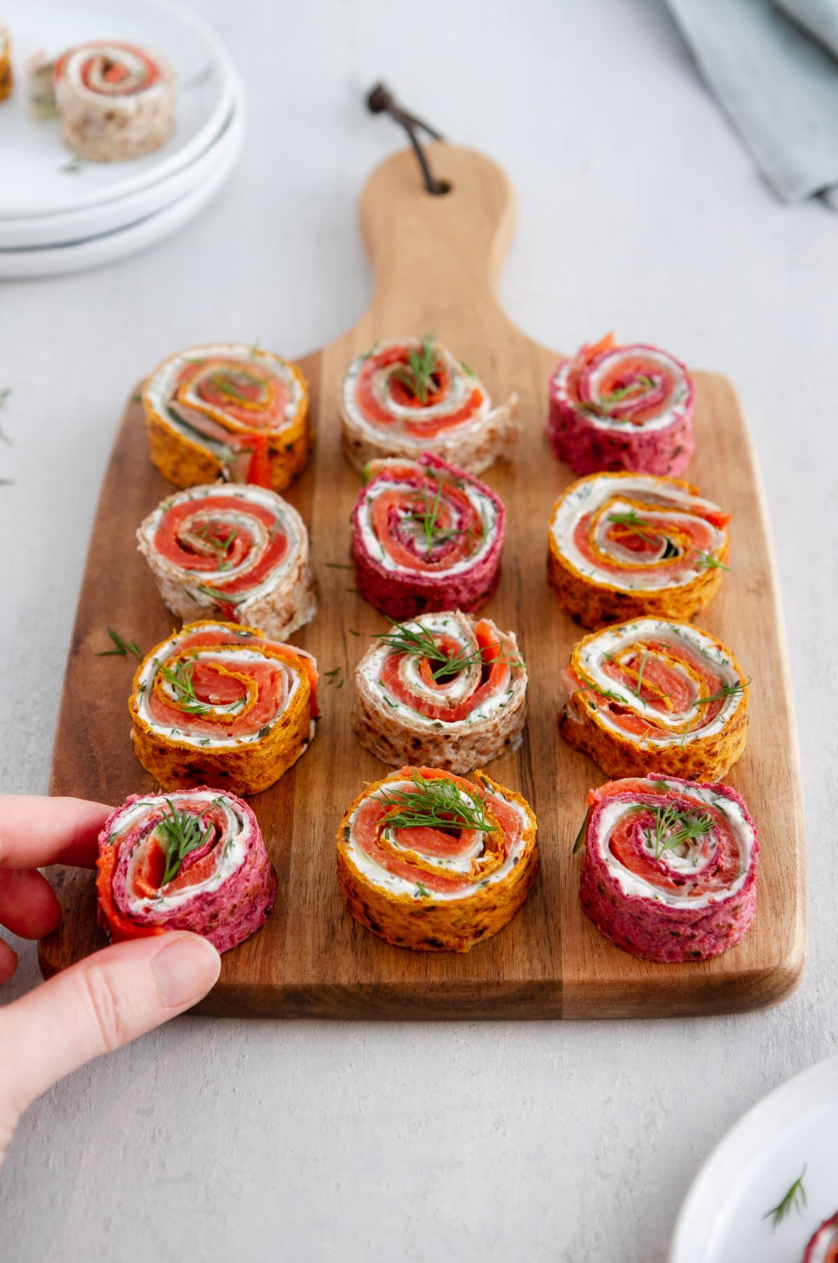 a hand grabbing a salmon pinwheel from a cutting board