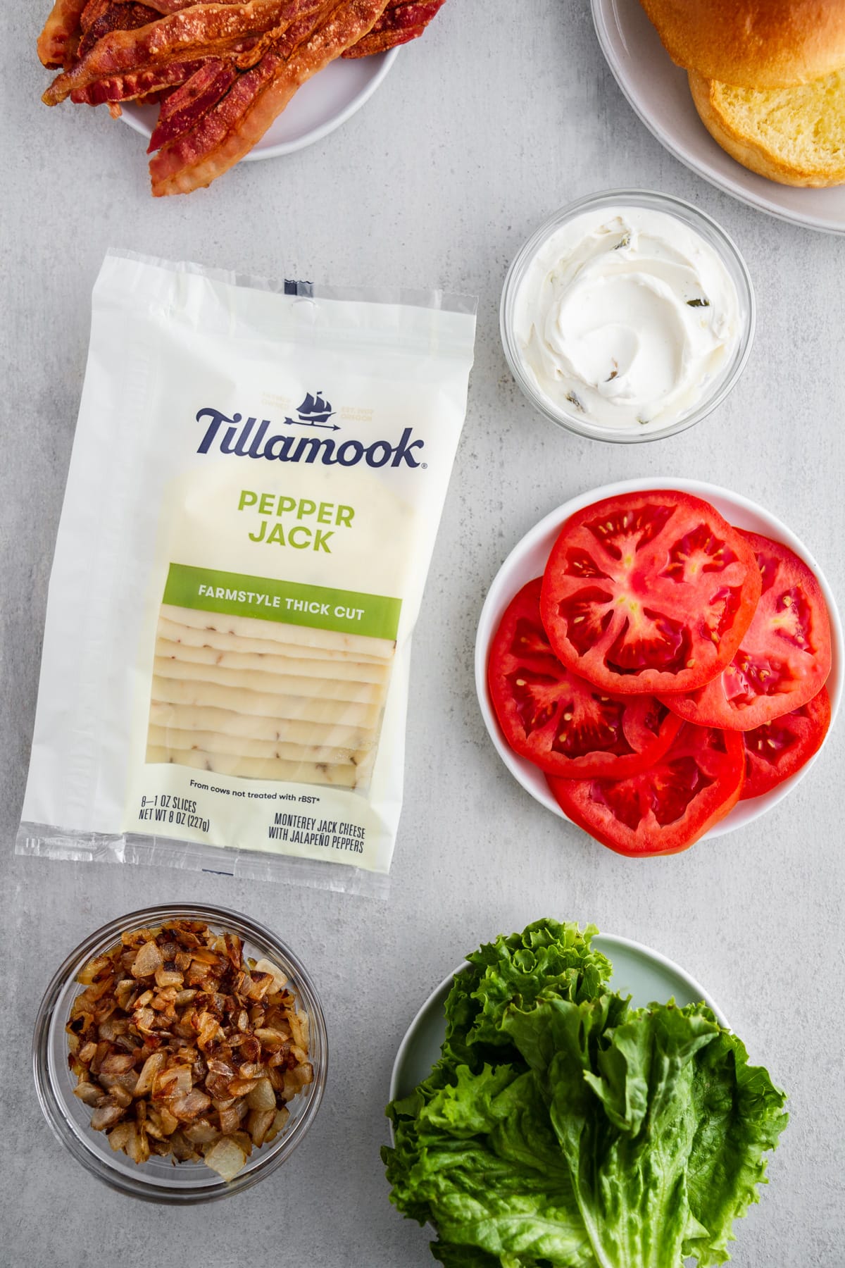 an overhead shot of Tillamook Pepper Jack cheese slices, tomatoes, cream cheese, bacon, onions and lettuce on plates