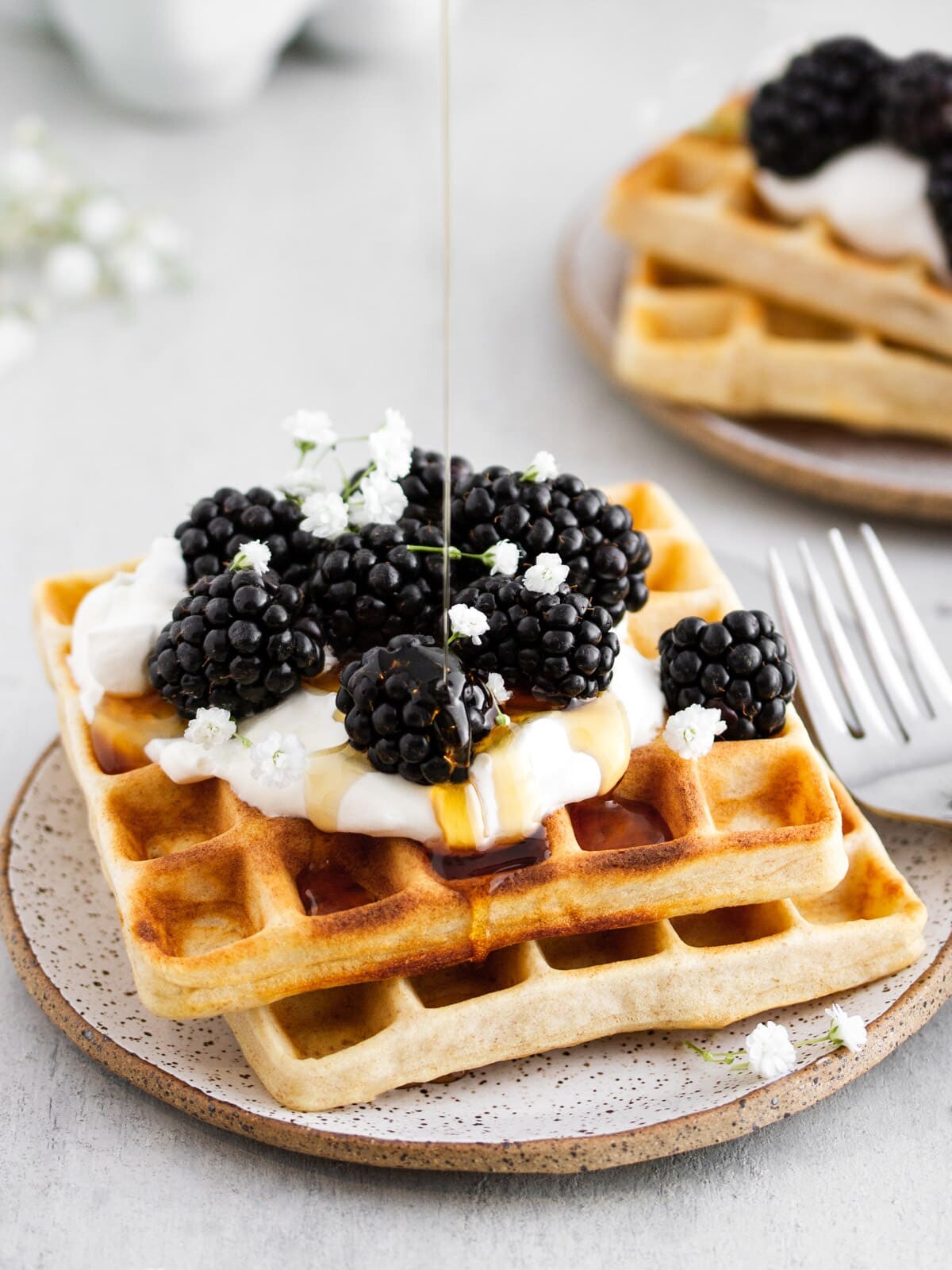 maple syrup being drizzled onto sourdough waffles on a plate.