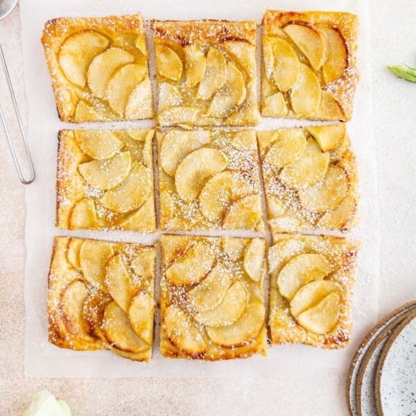 French apple tart cut up on a surface.