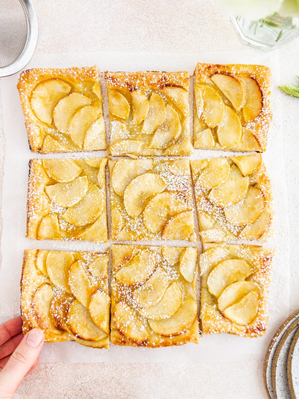 a hand removing a slice of French apple tart on a surface
