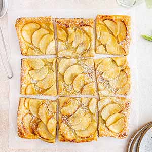French apple tart cut up on a surface.