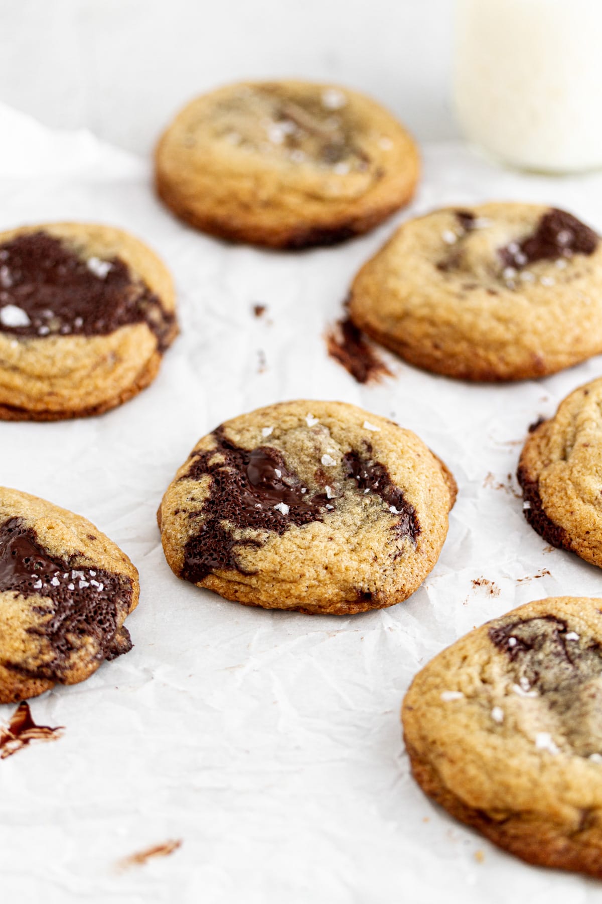 chocolate chip cookies on parchment paper with a glass of milk in the background