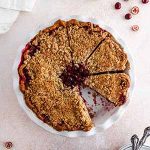 cranberry crumble pie on a surface with a slice taken out.
