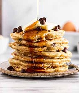 pouring maple syrup on a stack of oatmeal chocolate chip pancakes