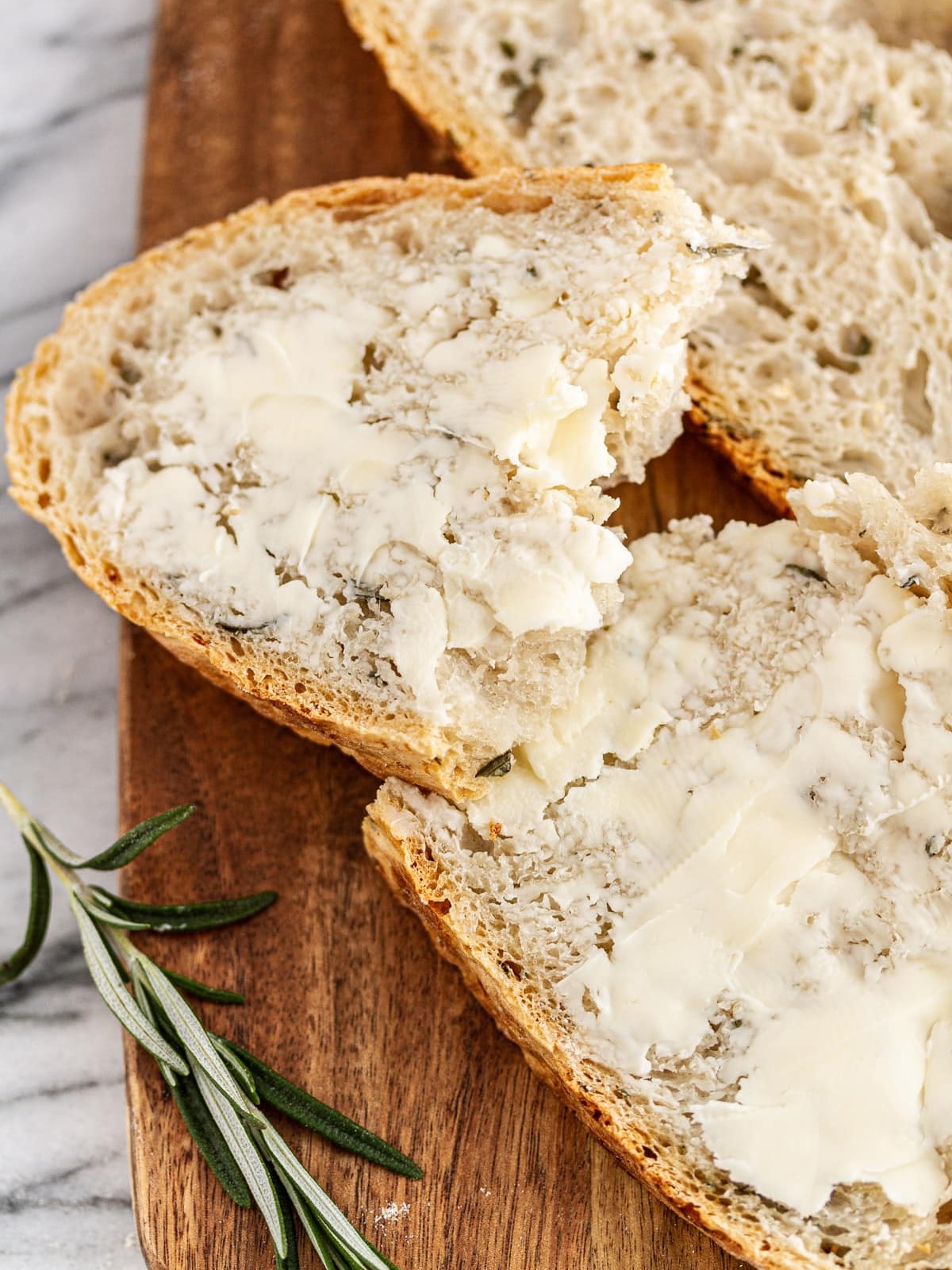 buttered slice of rosemary garlic bread on wooden board.