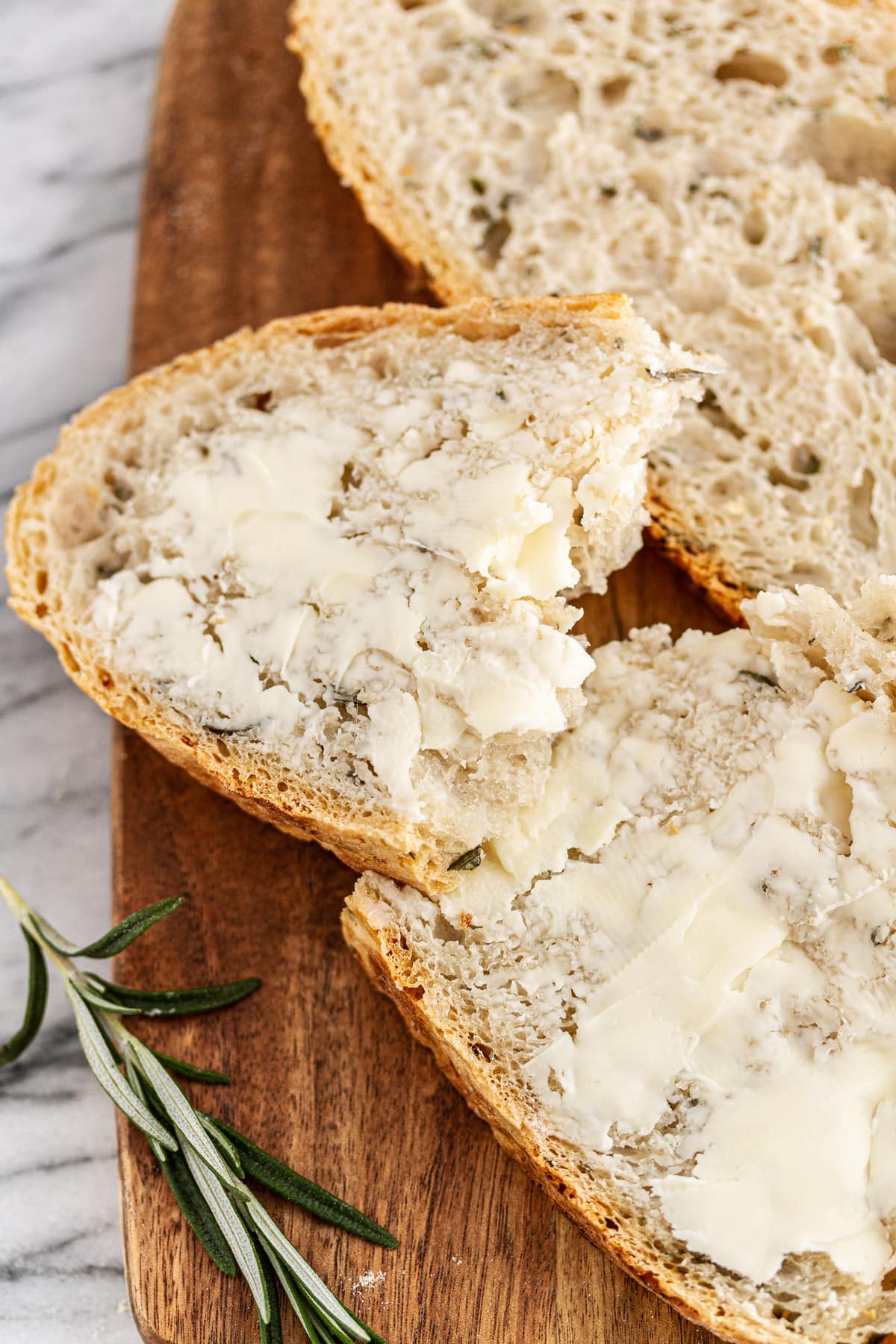 buttered slice of rosemary-garlic no-knead bread on a cutting board