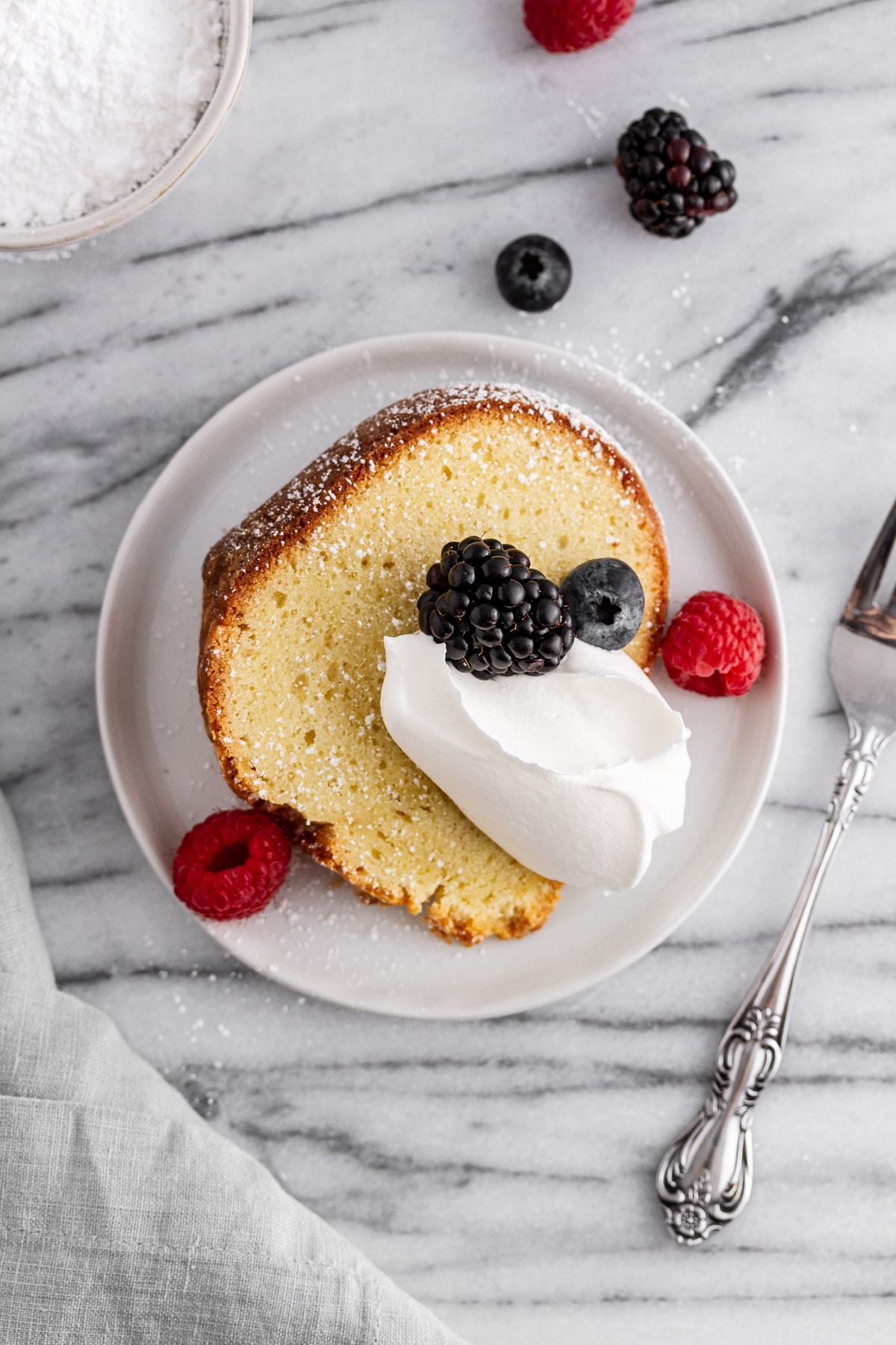 slice of sour cream pound cake on a plate with whipped cream and berries