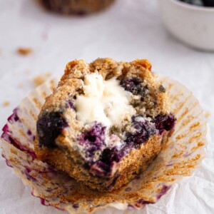 half of a sourdough blueberry muffin with butter on parchment paper