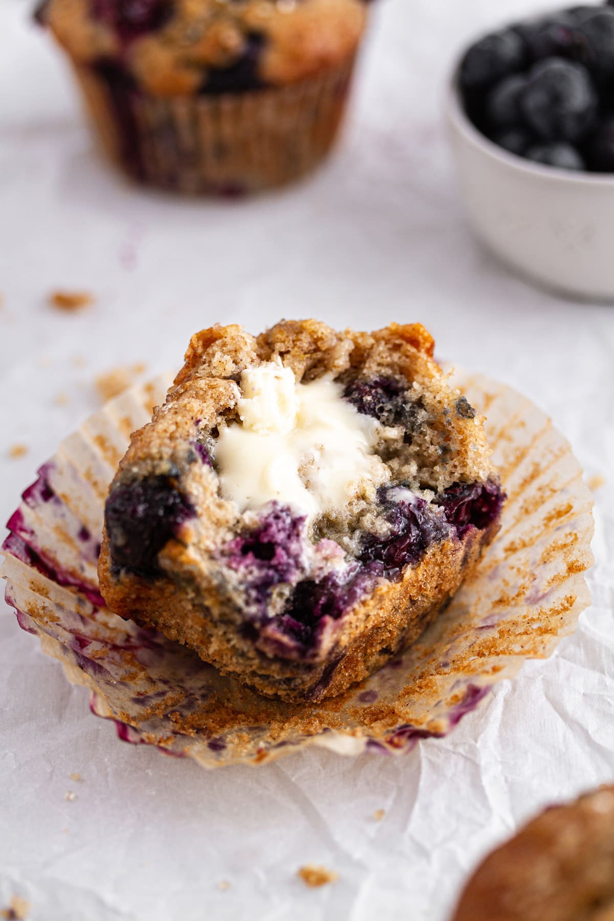 half of a sourdough blueberry muffin with butter on parchment paper