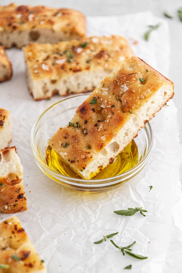 slice of sourdough focaccia dipped into a bowl of olive oil