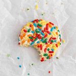 confetti cookie on parchment paper with a bite taken out of it.