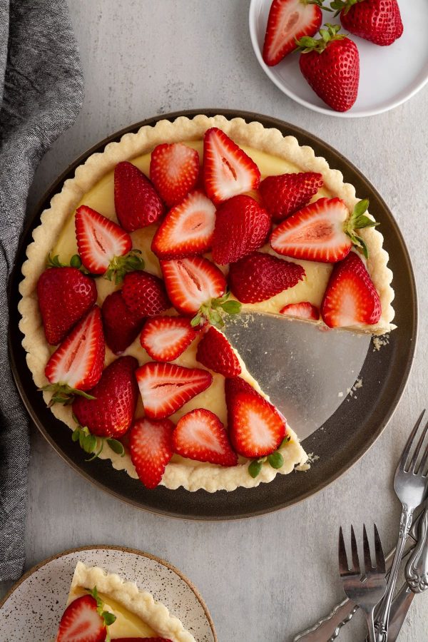 strawberry custard tart on a plate with a slice taken out of it