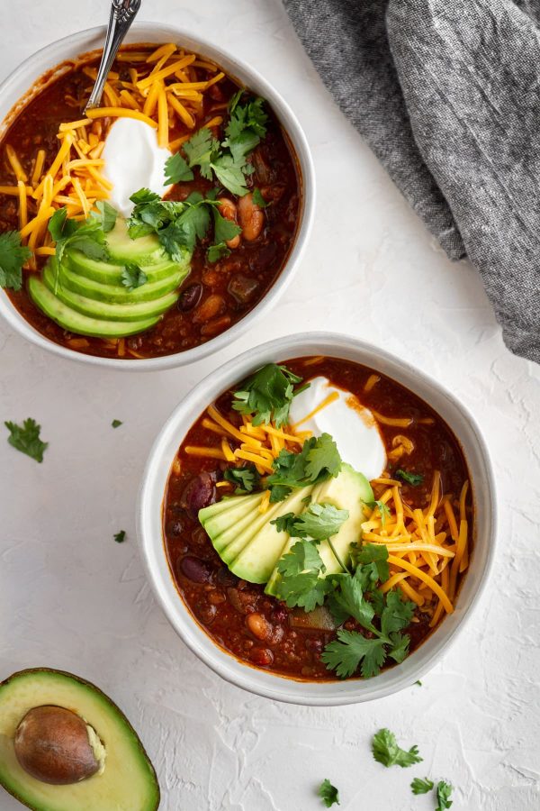 two bowls of beef and red wine chili with toppings