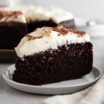 slice of guinness chocolate cake on grey plate with cream cheese frosting.