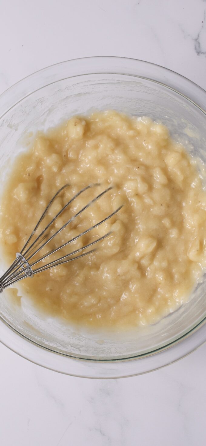 Mashed bananas in bowl with whisk.