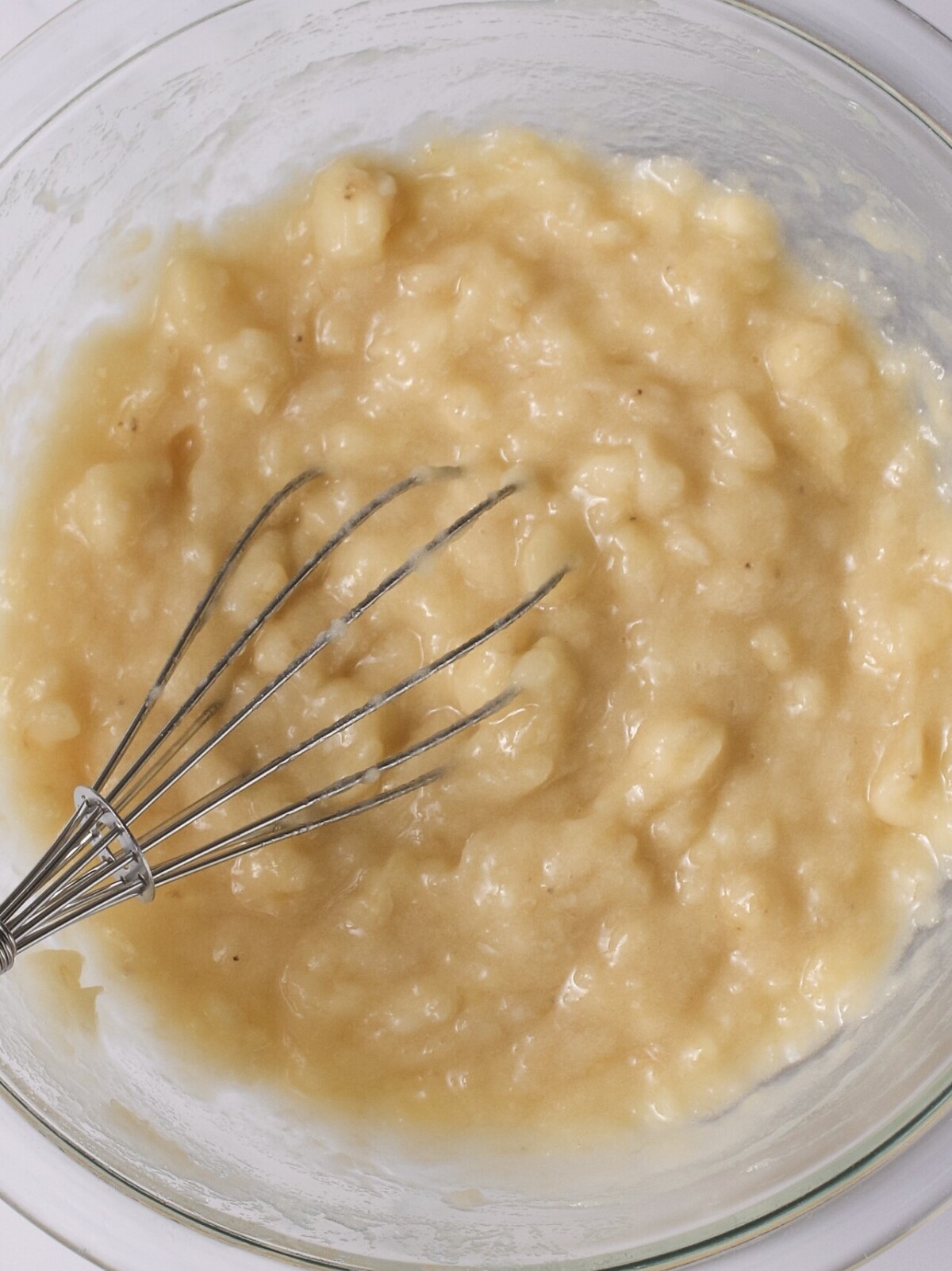Mashed bananas in bowl with whisk.