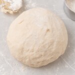 pizza dough ball on floured white countertop.