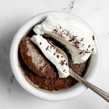pot de creme with whipped cream on half with a spoon dipping in.