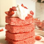 4 stacked strawberry brownies with whipped cream and strawberries on top.