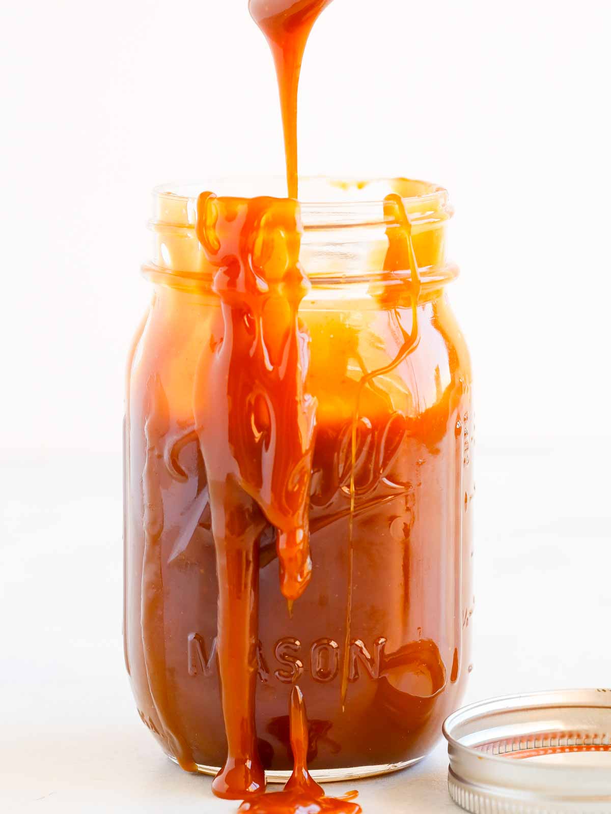 salted caramel sauce pouring off spoon into jar.