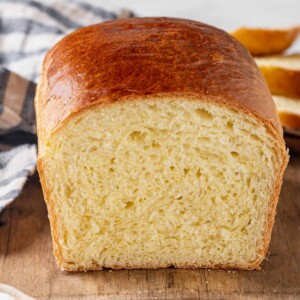 baked brioche sliced open to show interior crumb on wooden board with napkin.