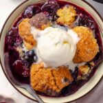 Cherry cobbler with melting ice cream in a bowl.