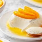 vanilla bean panna cotta on white plate with bite on gold spoon.