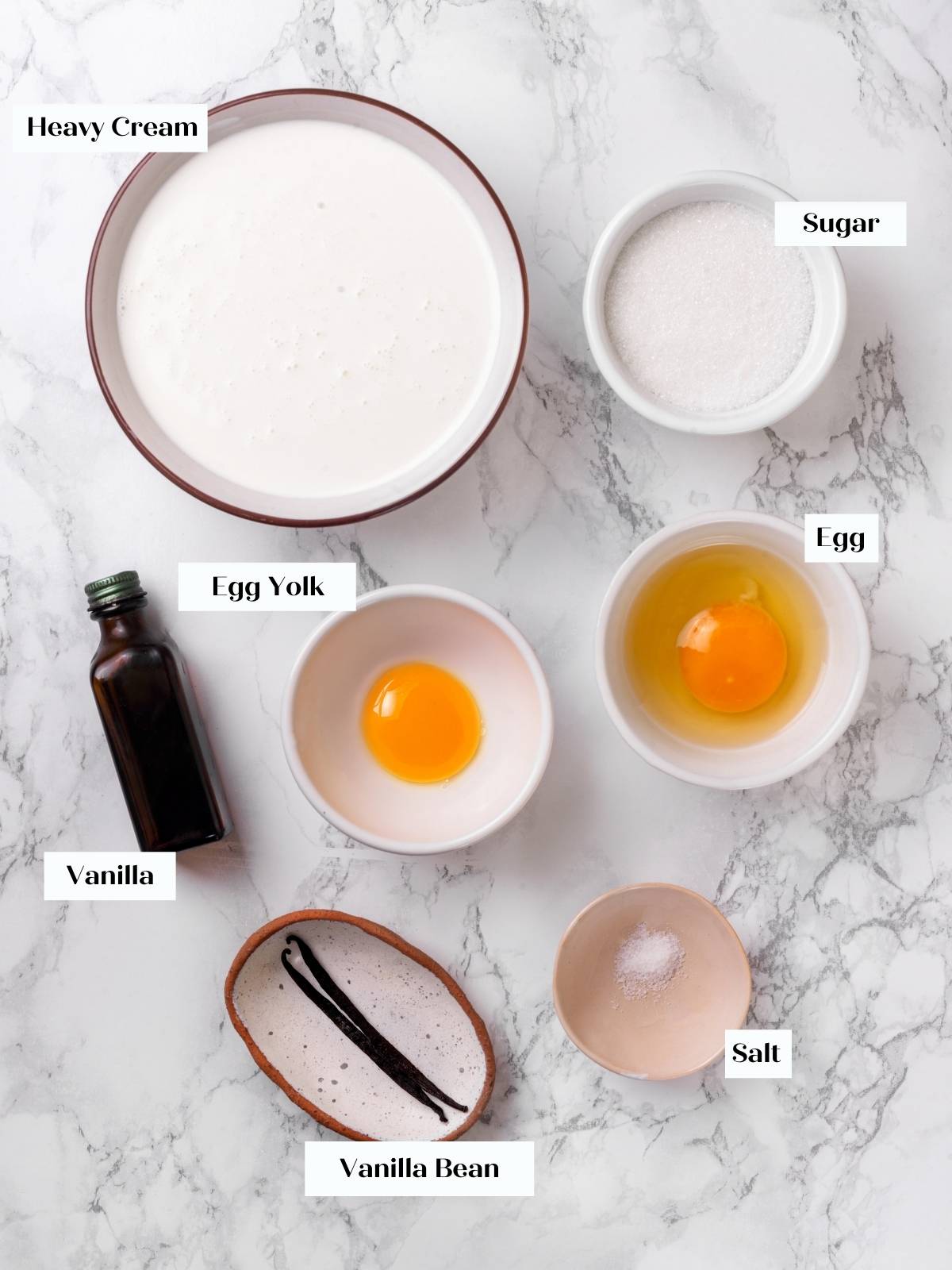 Ingredients for creme brulee, including eggs, cream, and sugar, arranged on a white marble surface.