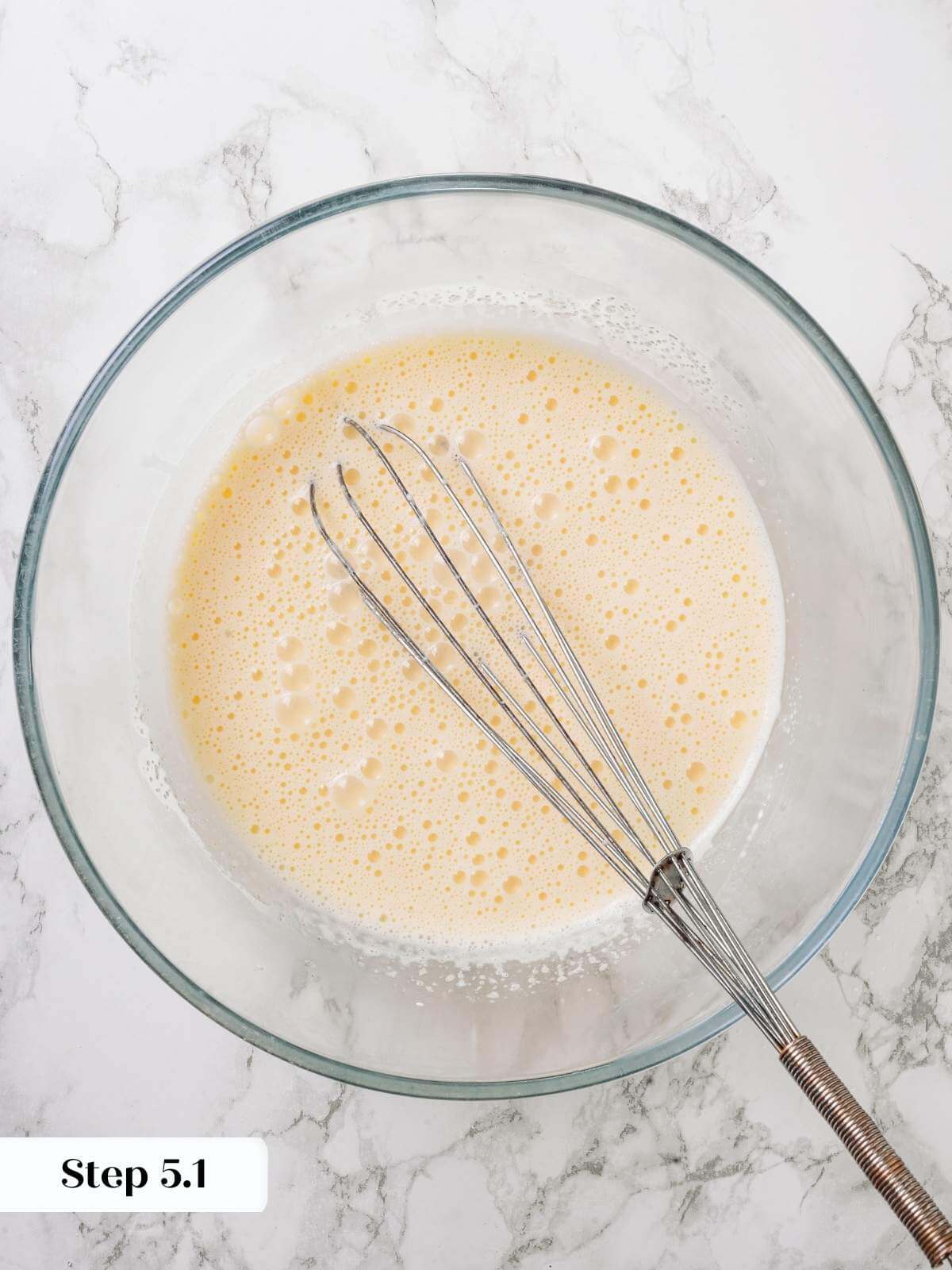 Creme brulee custard mixture being whisked together in a clear mixing bowl.