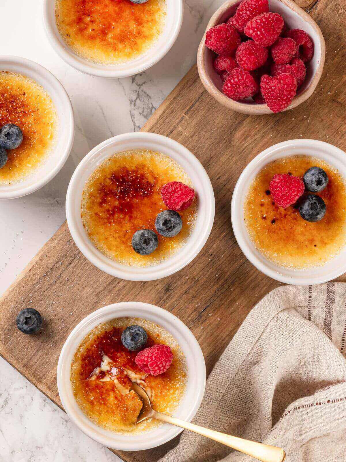 Creme brulee served on a rustic wooden cutting board with caramelized sugar glistening on top.