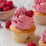 Raspberry cupcakes topped with frosting and garnished with fresh raspberries.