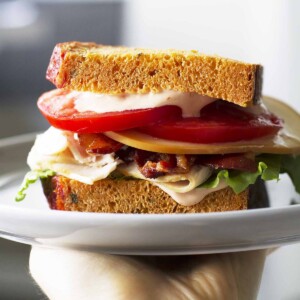 homemade bacon turkey bravo sandwich on white plate in hand.