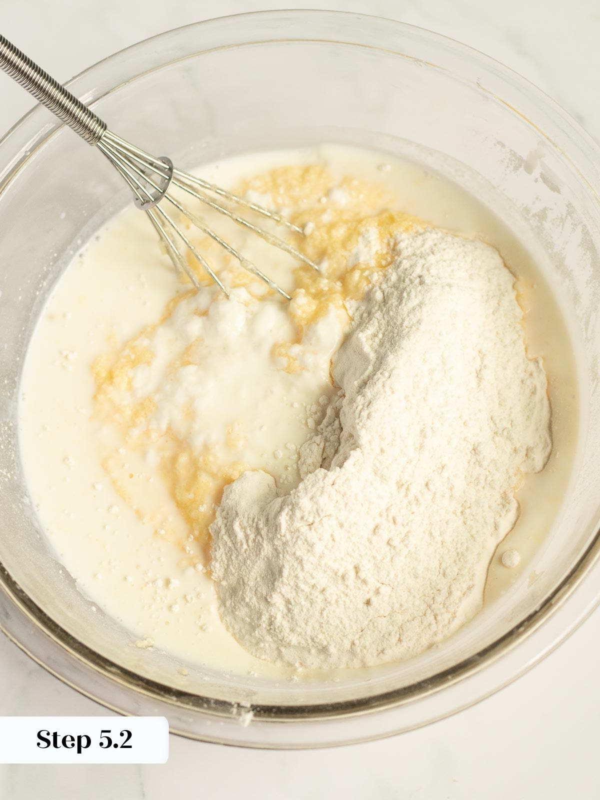 flour, baking powder, and salt being added to the wet batter in mixing bowl.