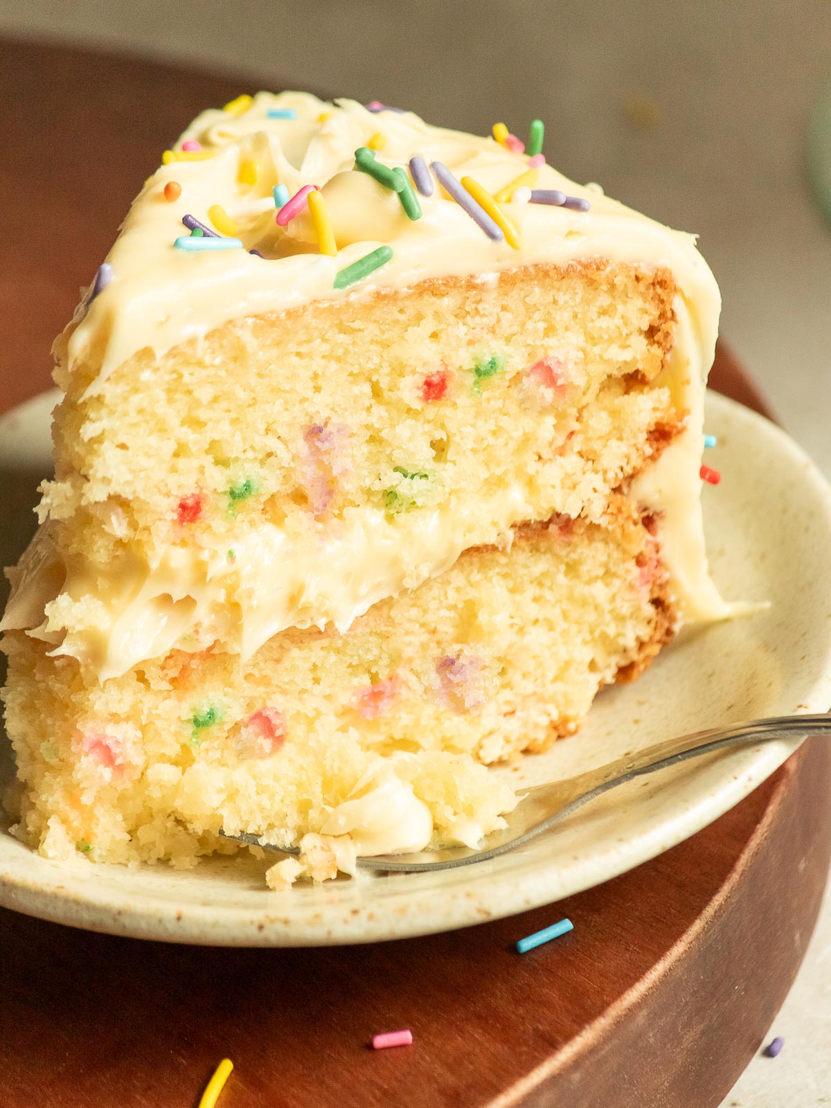 Two-layer funfetti cake piece with smooth buttercream and rainbow sprinkles.