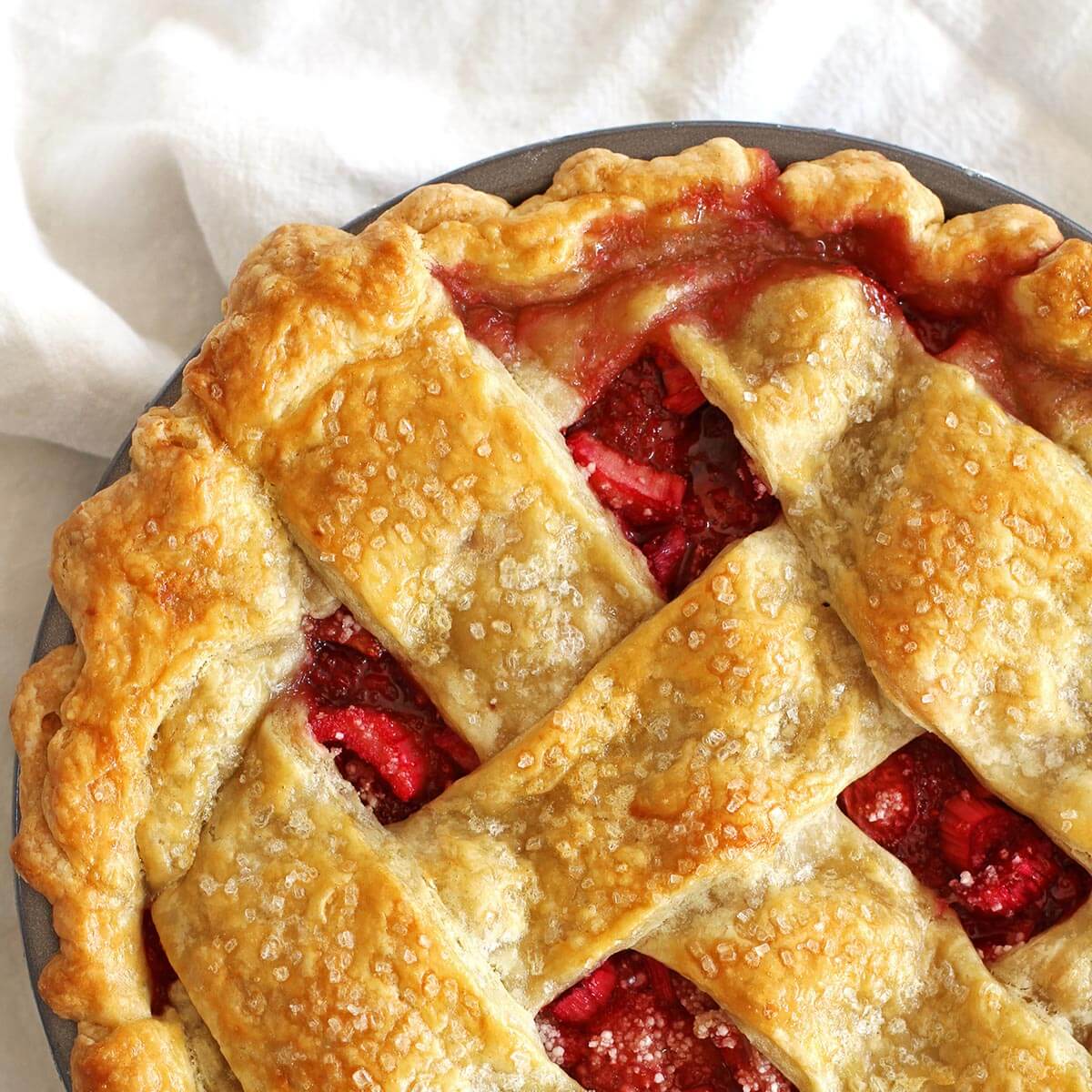 Whole strawberry rhubarb pie fresh out of the oven with bubbling fruit.