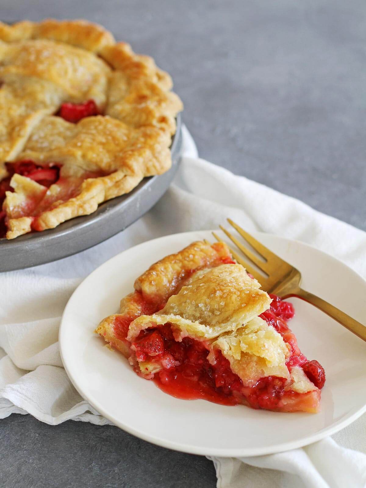 Slice of strawberry rhubarb pie with thick filling and flaky crust on a plate.