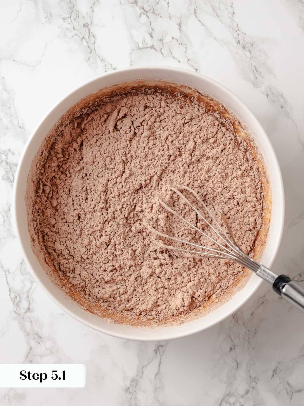 Pouring flour and cocoa into wet ingredients to complete the chocolate donut mix.
