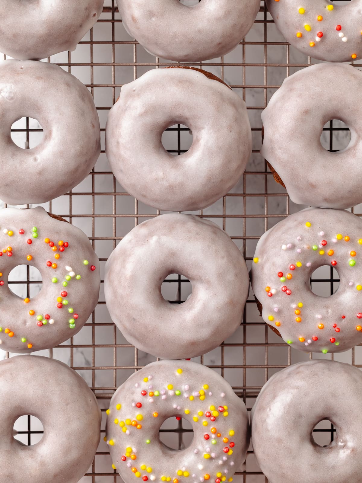 A mix of chocolate donuts, some glazed plainly and others topped with colorful sprinkles.