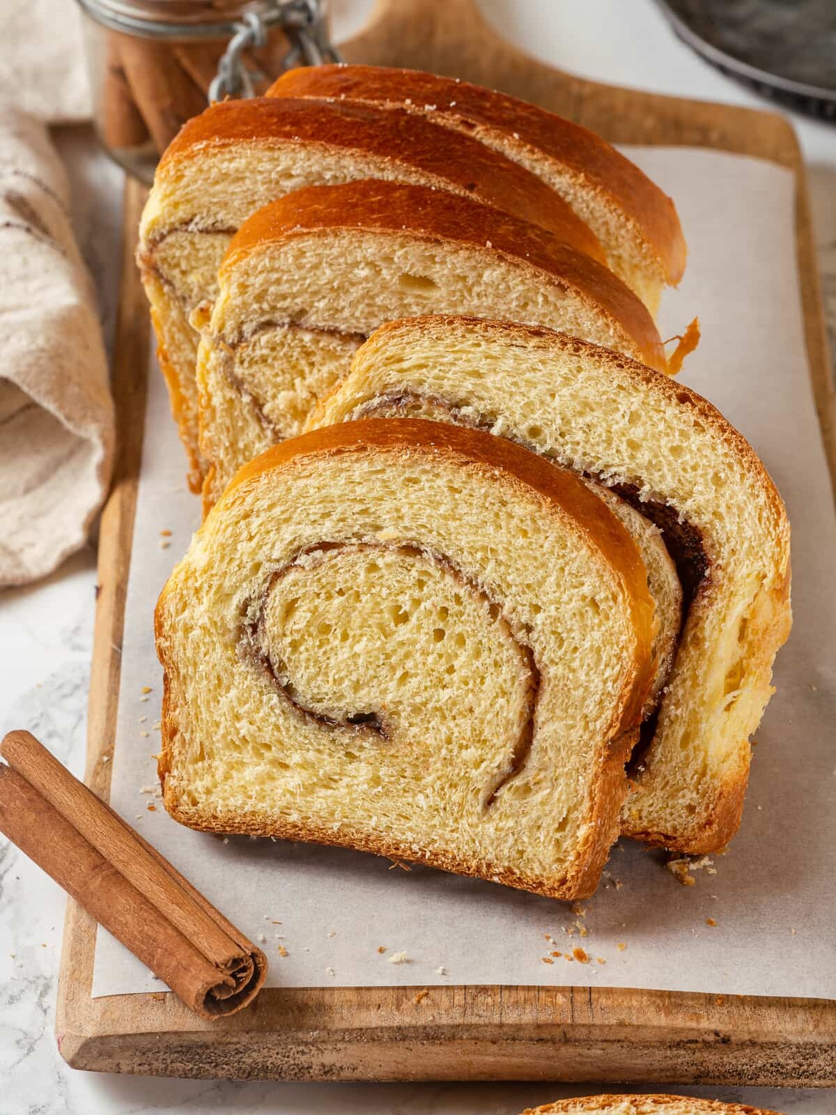 Slices of cinnamon swirl bread beside whole cinnamon sticks to emphasize the warm spice.