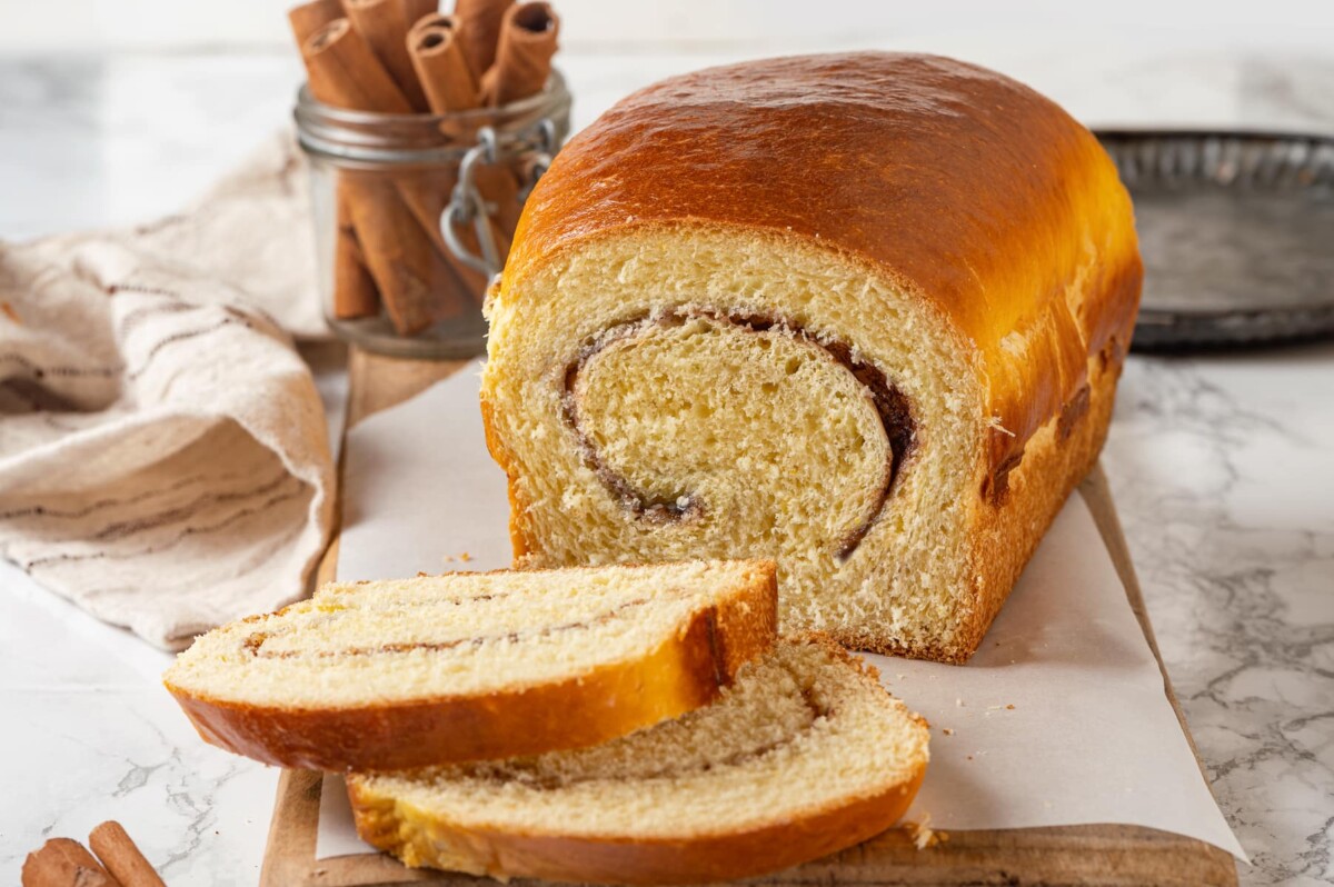 Finished cinnamon swirl bread sits on a marble surface, showing even crust and light shine.